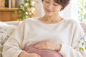 ソファで温かいクッションをお腹に当て、ほっとする女性