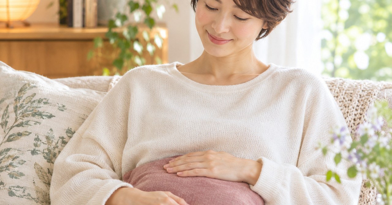 ソファで温かいクッションをお腹に当て、ほっとする女性