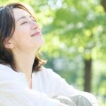 木漏れ日の下で目を閉じ、深呼吸する女性