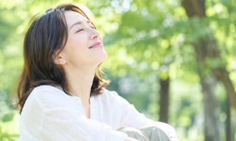 木漏れ日の下で目を閉じ、深呼吸する女性