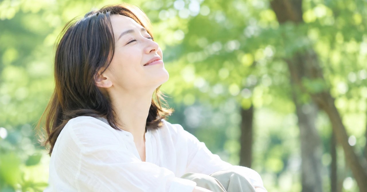 木漏れ日の下で目を閉じ、深呼吸する女性